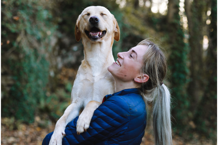 A blonde dog owner holds her blonde haired dog. Both look very happy.